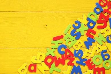 Photo of Learning alphabet. Magnetic letters on yellow wooden background, flat lay. Space for text