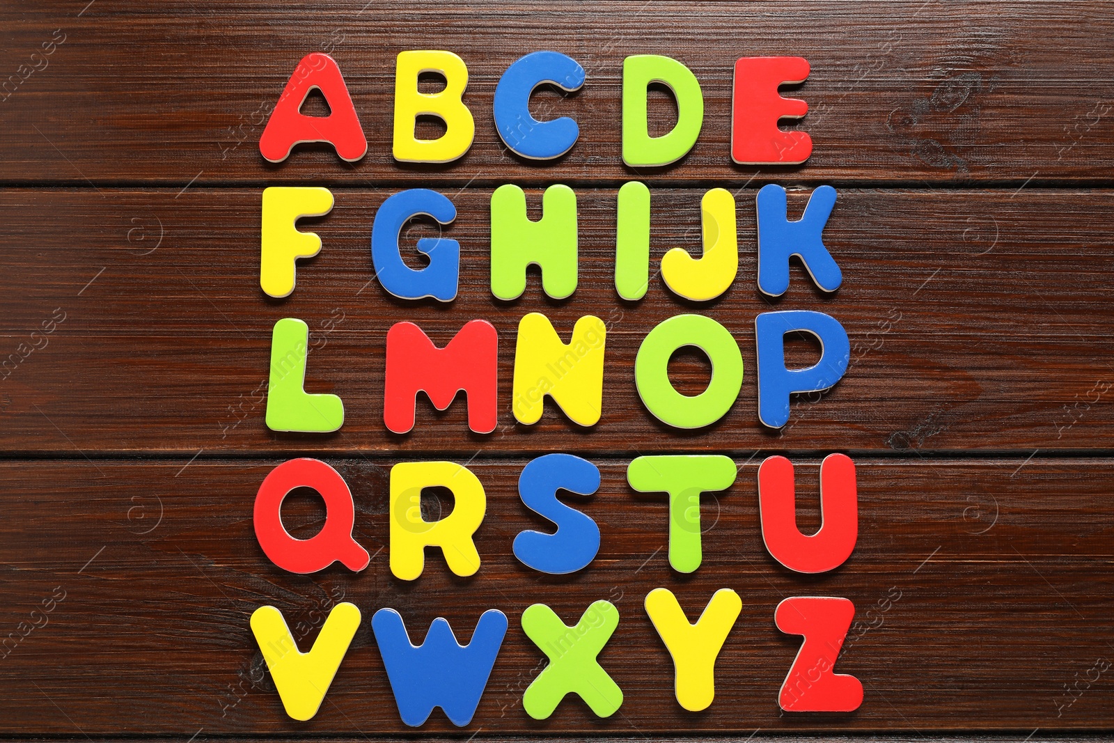 Photo of Alphabetical order. Bright magnetic letters on wooden background, top view