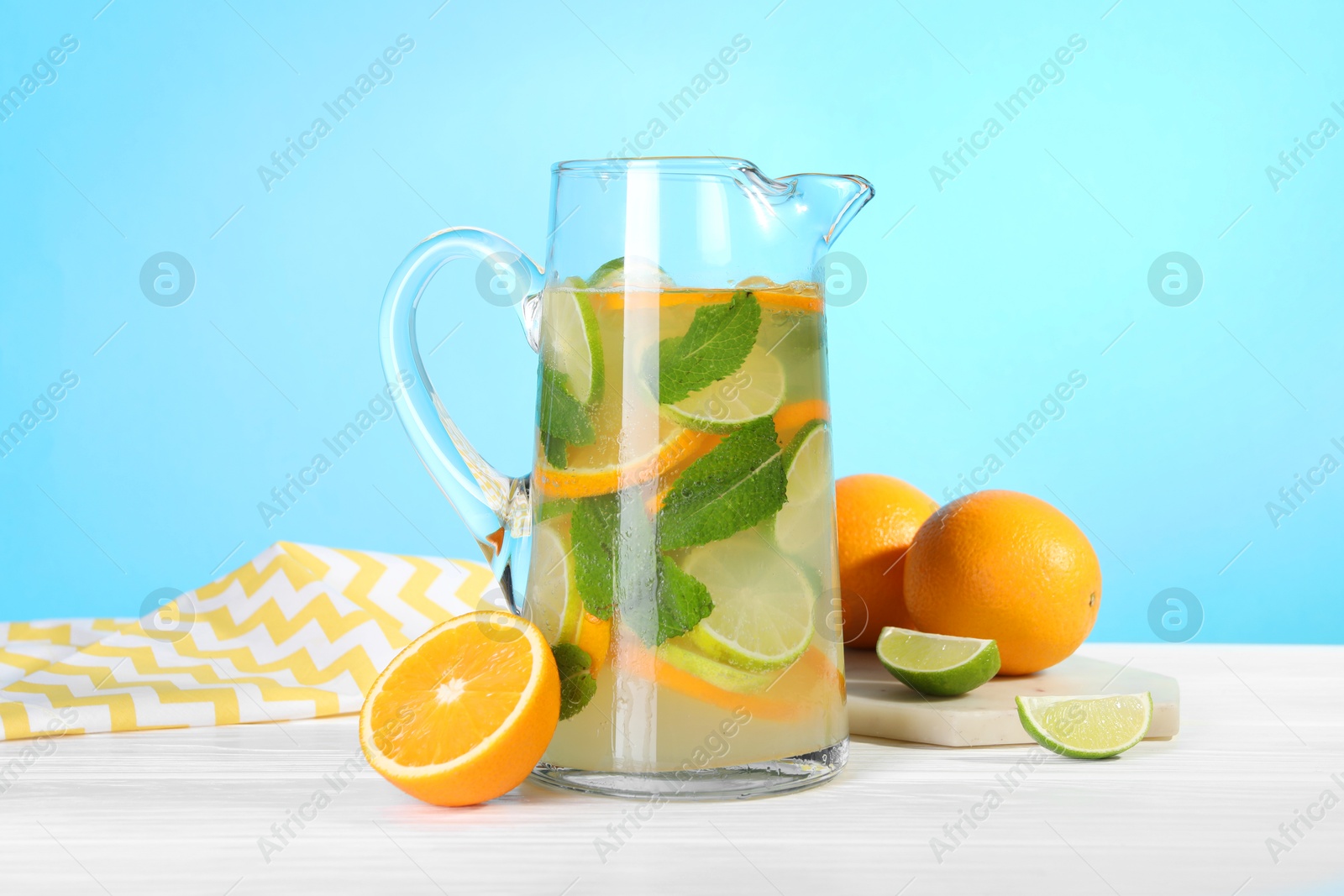 Photo of Freshly made lemonade with mint in jug on white wooden table against light blue background