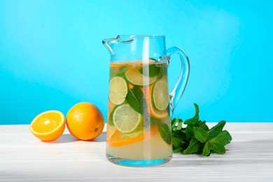 Photo of Freshly made lemonade with mint in jug on white wooden table against light blue background