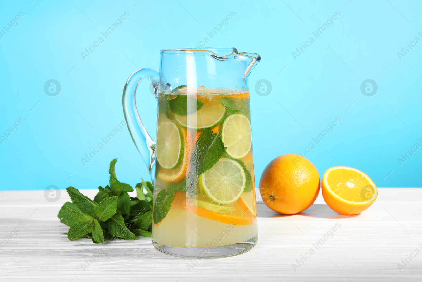 Photo of Freshly made lemonade with mint in jug on white wooden table against light blue background