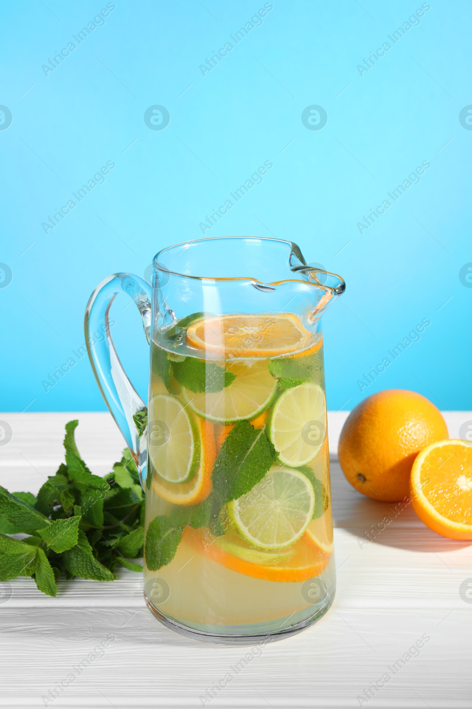 Photo of Freshly made lemonade with mint in jug on white wooden table against light blue background