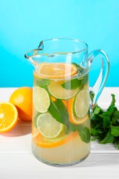 Photo of Freshly made lemonade with mint in jug on white wooden table against light blue background