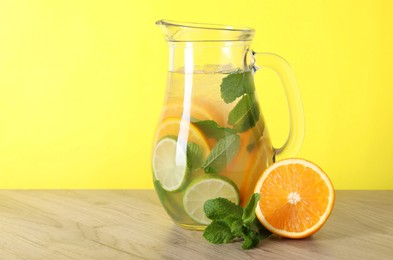 Photo of Freshly made lemonade with mint in jug on wooden table against yellow background