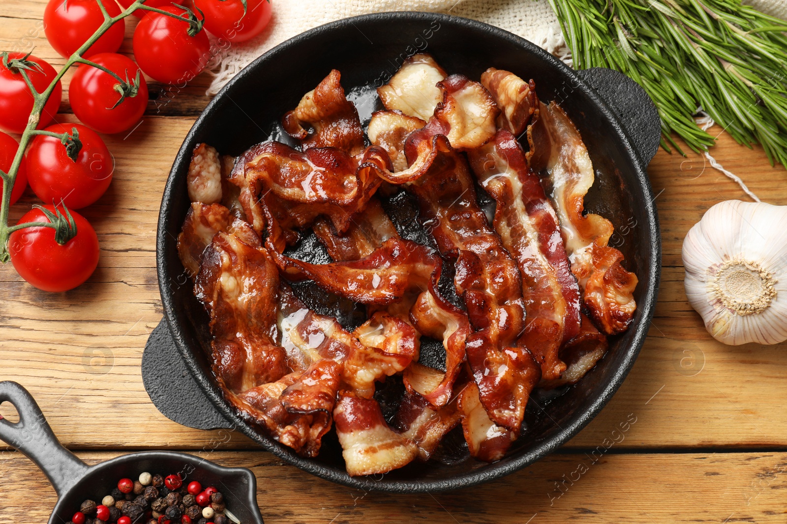 Photo of Delicious bacon slices in frying pan and products on wooden table, flat lay