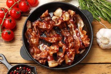 Delicious bacon slices in frying pan and products on wooden table, flat lay