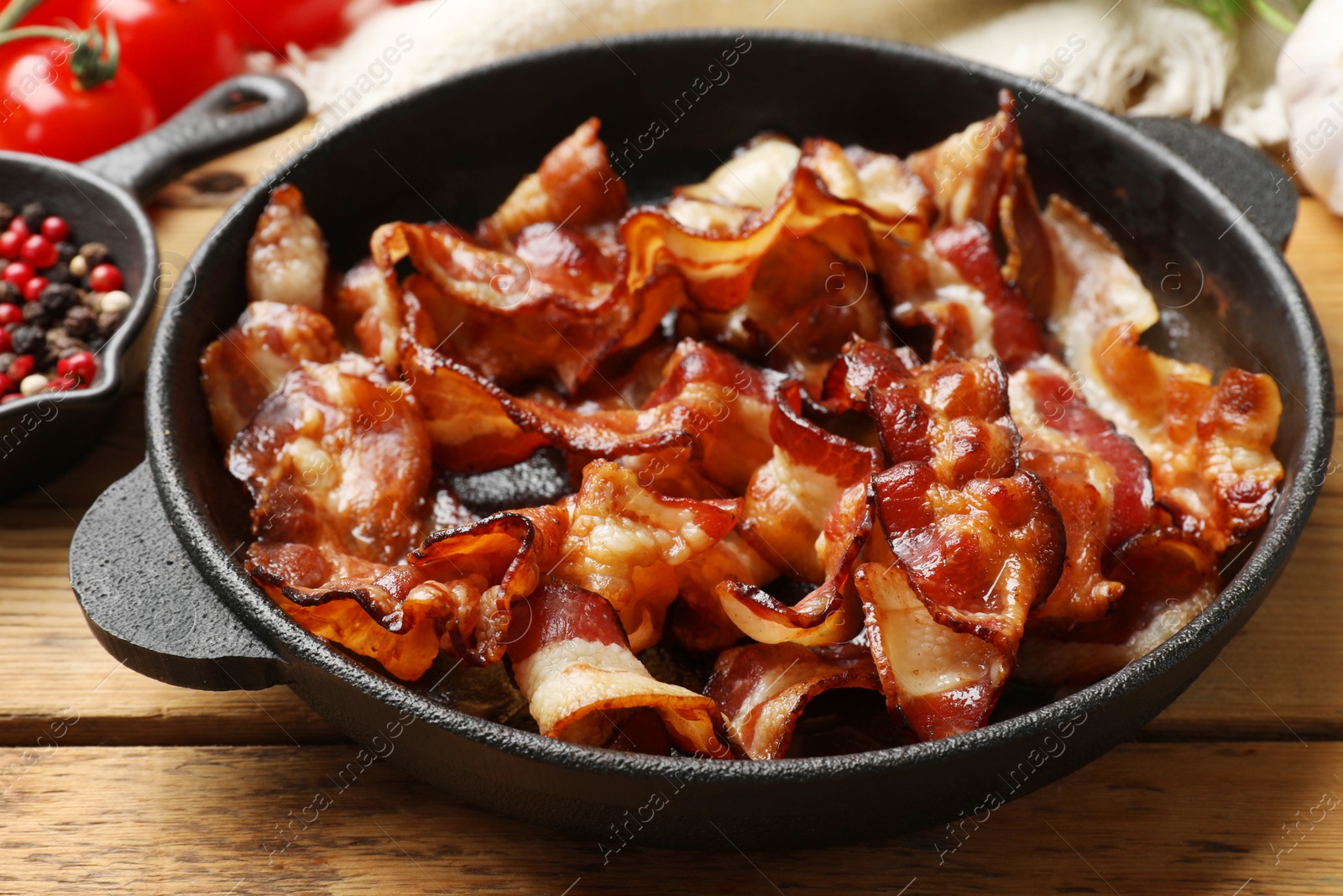 Photo of Delicious bacon slices in frying pan and products on wooden table, closeup