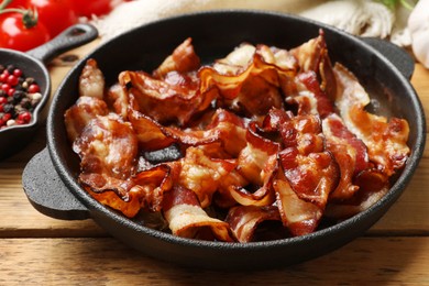 Delicious bacon slices in frying pan and products on wooden table, closeup