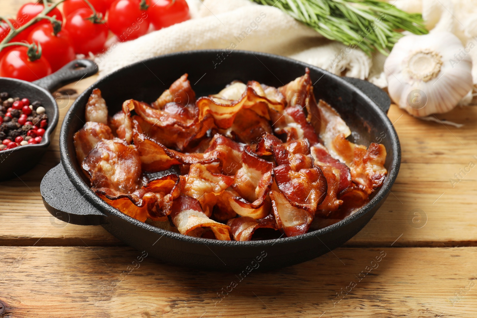 Photo of Delicious bacon slices in frying pan and products on wooden table