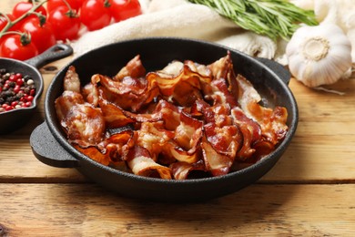 Delicious bacon slices in frying pan and products on wooden table