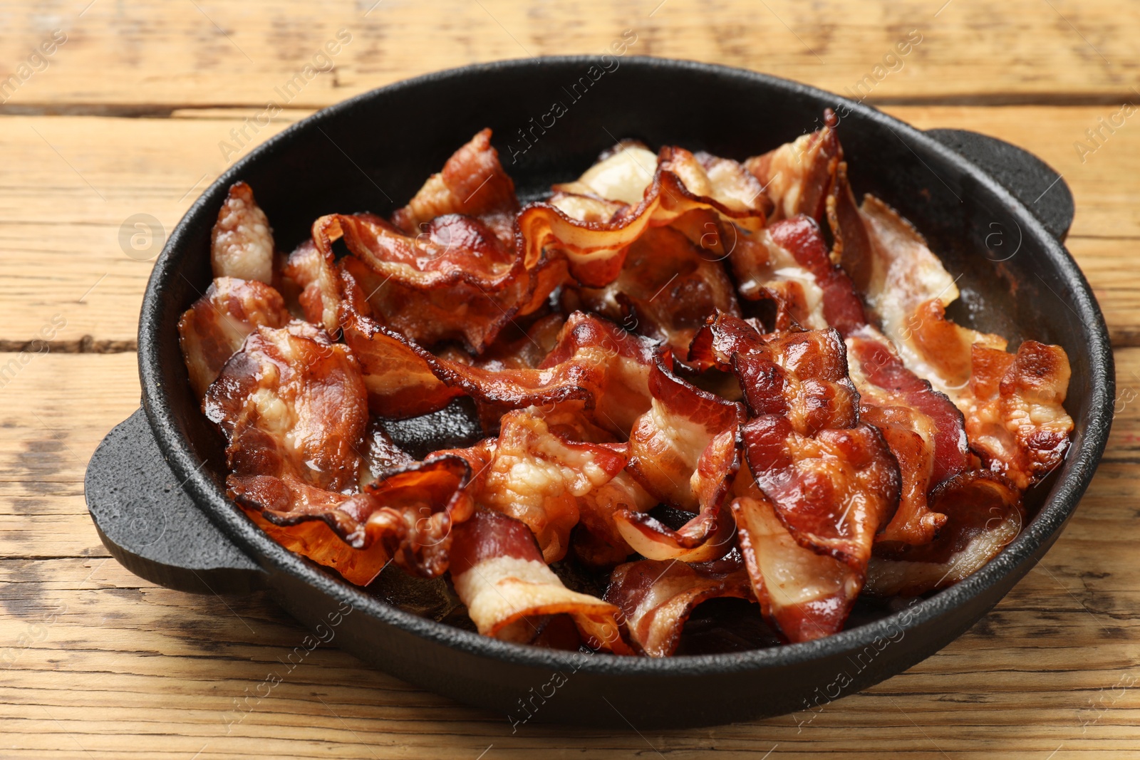 Photo of Delicious bacon slices in frying pan on wooden table, closeup