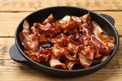 Photo of Delicious bacon slices in frying pan on wooden table, closeup