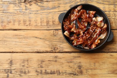 Delicious bacon slices in frying pan on wooden table, top view. Space for text