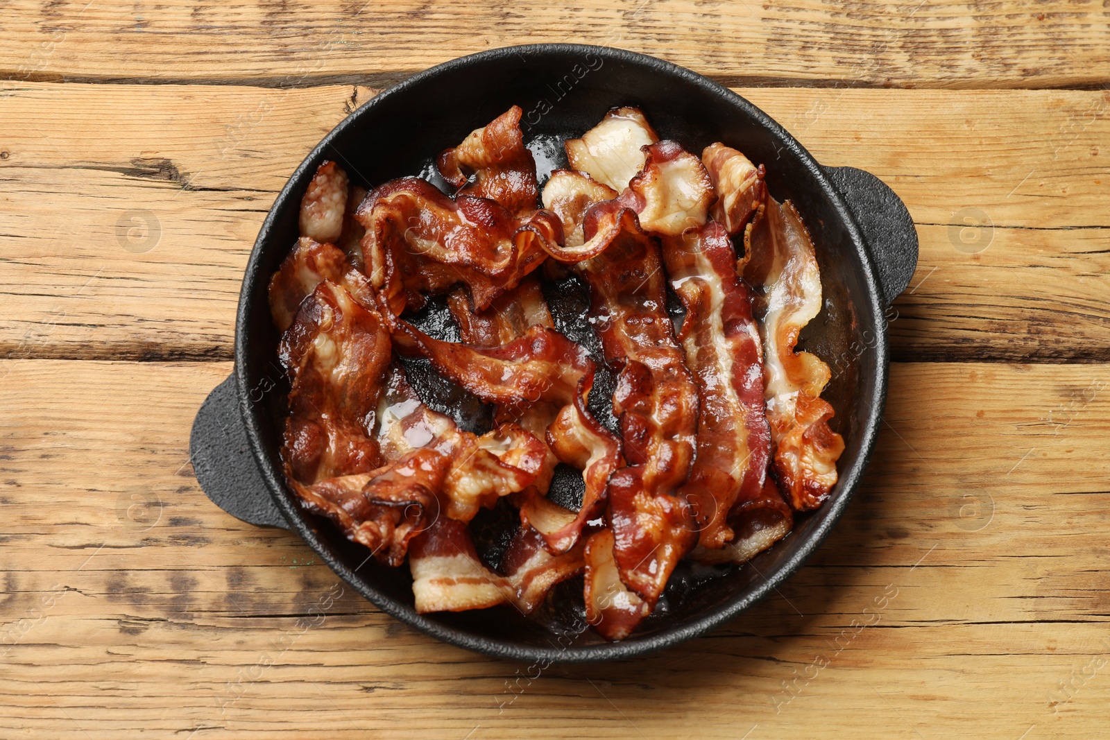 Photo of Delicious bacon slices in frying pan on wooden table, top view