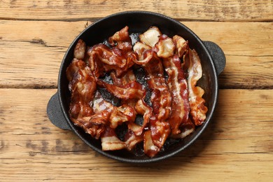 Delicious bacon slices in frying pan on wooden table, top view