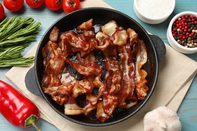 Delicious bacon slices in frying pan and products on light blue wooden table, flat lay