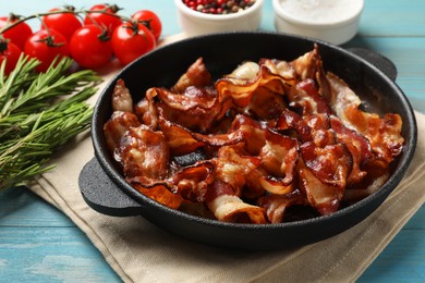 Photo of Delicious bacon slices in frying pan and products on light blue wooden table, closeup