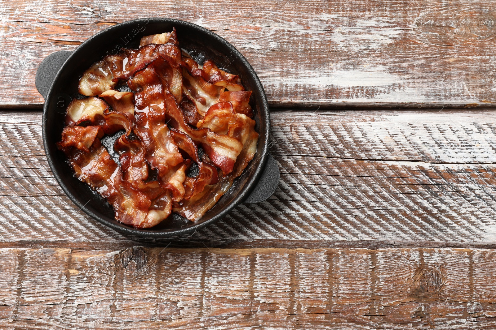 Photo of Delicious bacon slices in frying pan on wooden table, top view. Space for text