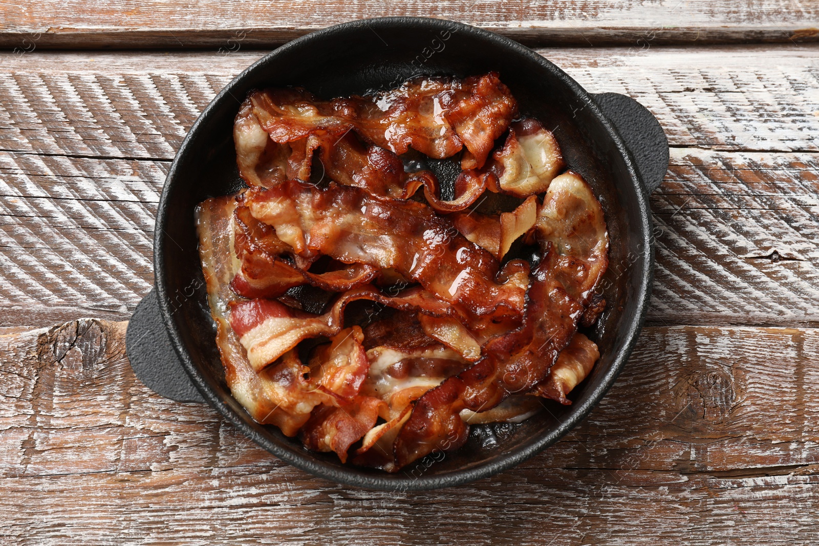 Photo of Delicious bacon slices in frying pan on wooden table, top view