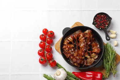 Photo of Delicious bacon slices in frying pan and products on white tiled table, flat lay. Space for text