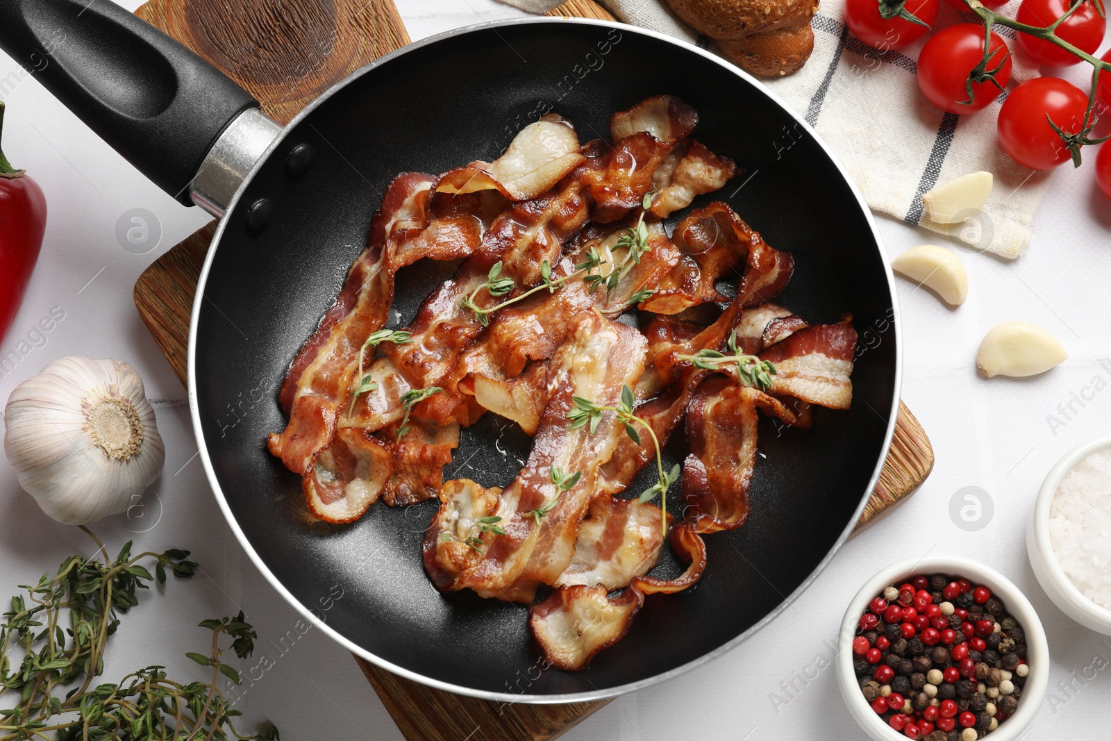 Photo of Delicious bacon slices in frying pan and products on white tiled table, flat lay