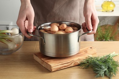 Photo of Woman holding pot with raw potatoes at wooden table, closeup