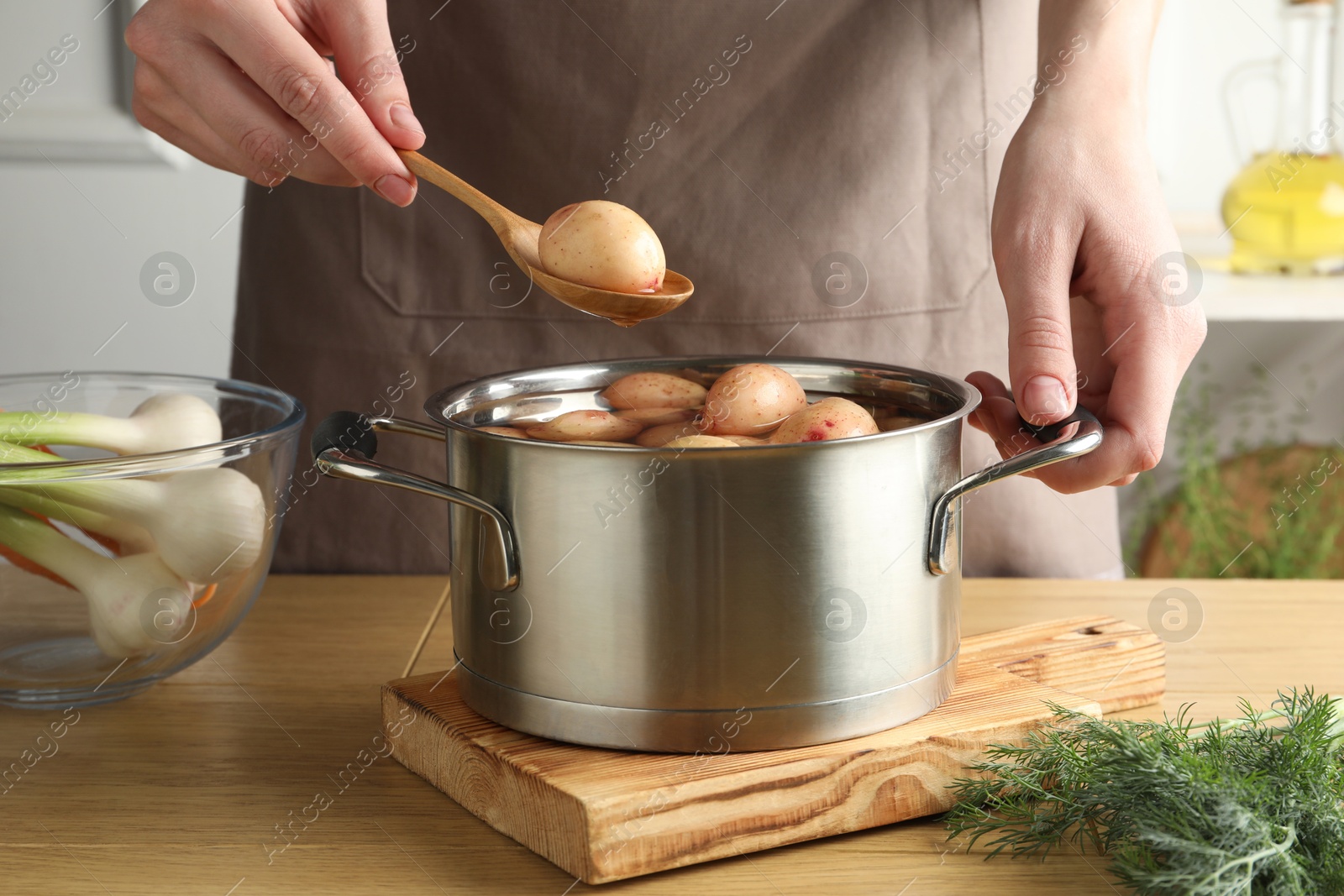 Photo of Woman putting raw potato into pot at wooden table, closeup