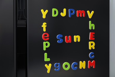 Word Sun and frame made of many bright magnetic letters on fridge indoors. Learning alphabet