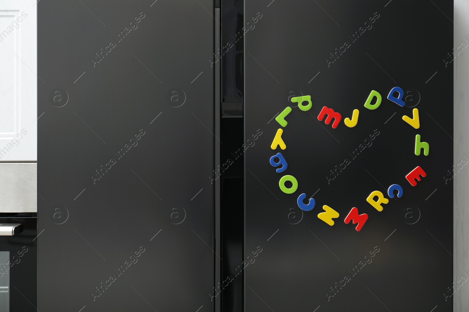 Photo of Heart made of many bright magnetic letters on fridge indoors. Learning alphabet