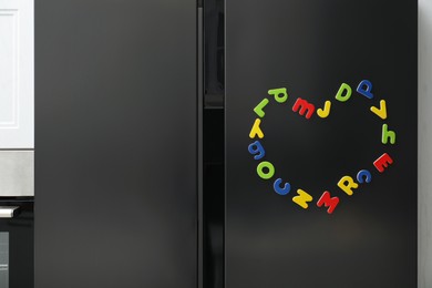 Photo of Heart made of many bright magnetic letters on fridge indoors. Learning alphabet