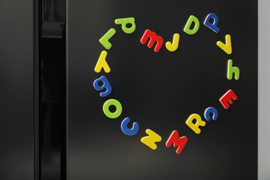 Heart made of many bright magnetic letters on fridge indoors. Learning alphabet