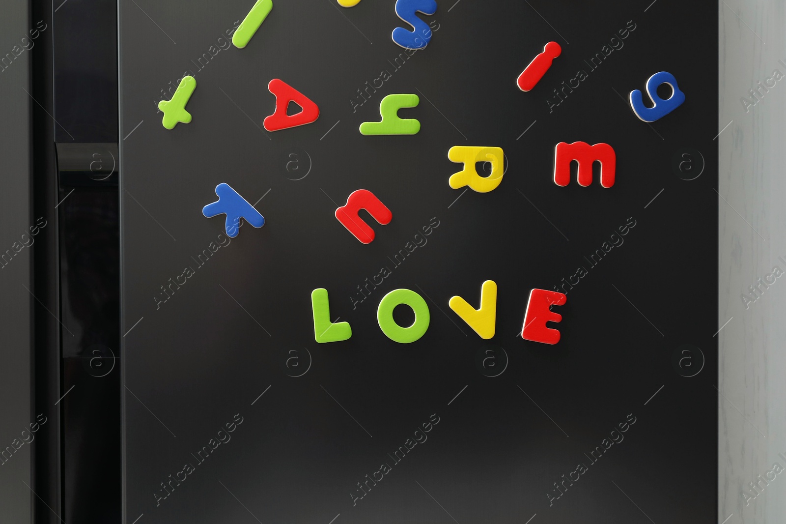 Photo of Word Love made of many bright magnetic letters on fridge indoors. Learning alphabet