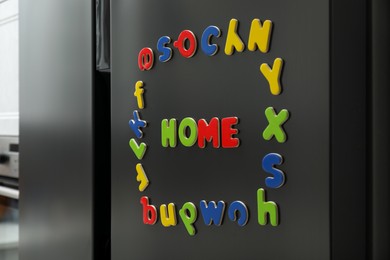 Photo of Word Home and frame made of many bright magnetic letters on fridge indoors. Learning alphabet