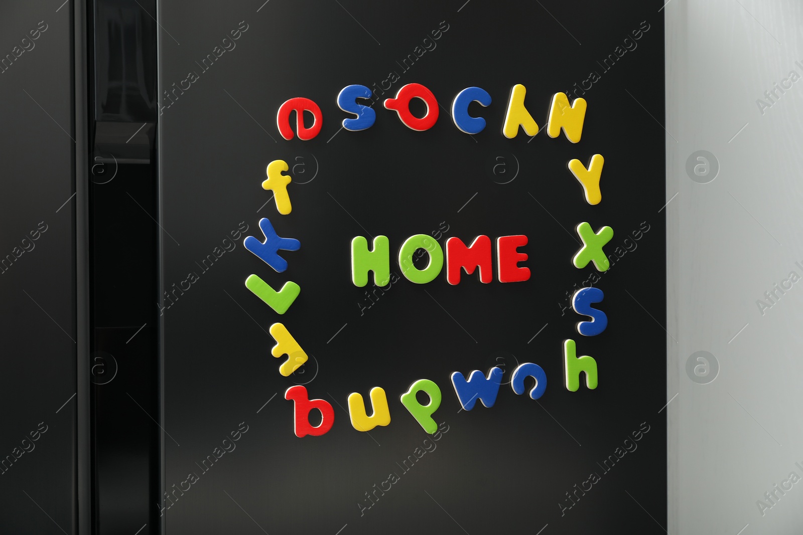 Photo of Word Home and frame made of many bright magnetic letters on fridge indoors. Learning alphabet