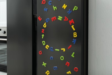 Many bright magnetic letters on fridge indoors. Learning alphabet