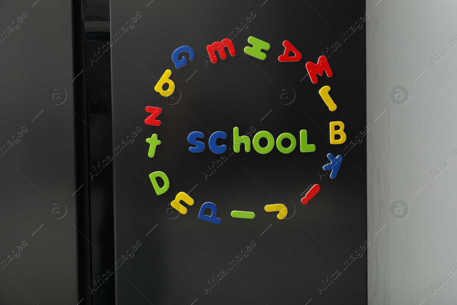 Photo of Word School and circle made of many bright magnetic letters on fridge indoors. Learning alphabet