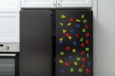 Many bright magnetic letters on fridge indoors. Learning alphabet