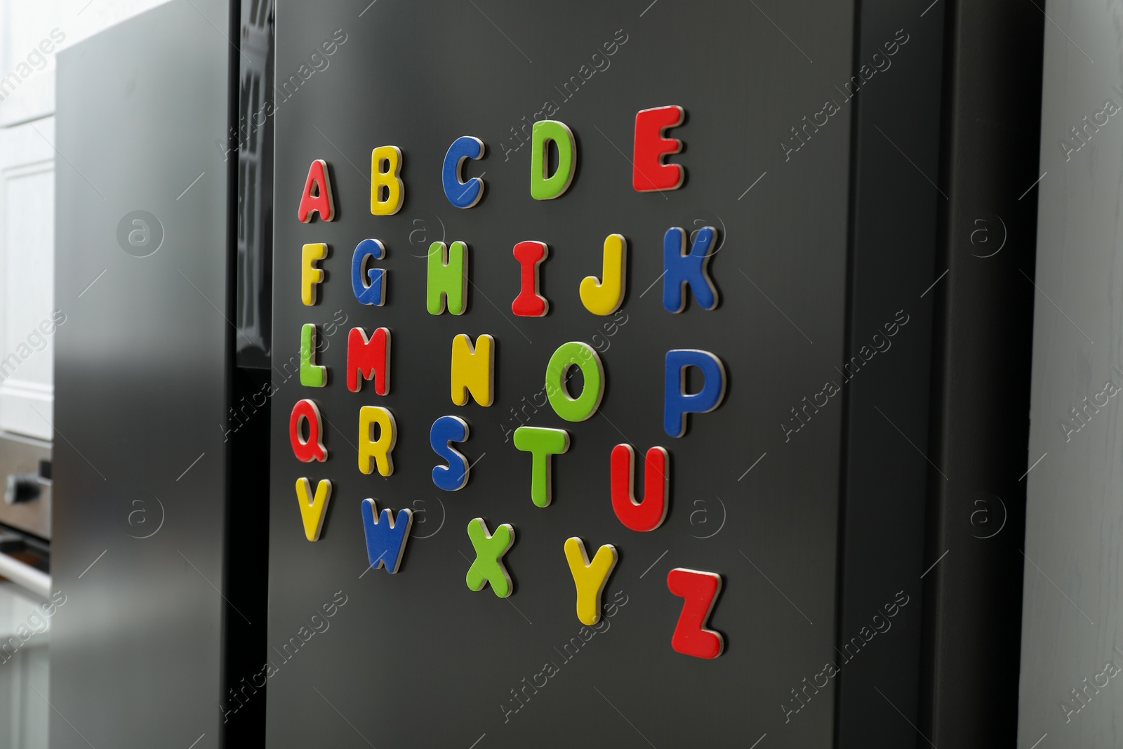 Photo of Alphabetical order. Many bright magnetic letters on fridge indoors