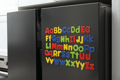 Photo of Alphabetical order. Many bright magnetic letters on fridge indoors