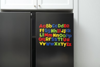 Photo of Alphabetical order. Many bright magnetic letters on fridge indoors