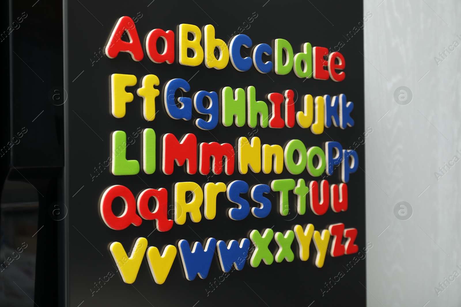 Photo of Alphabetical order. Many bright magnetic letters on fridge indoors