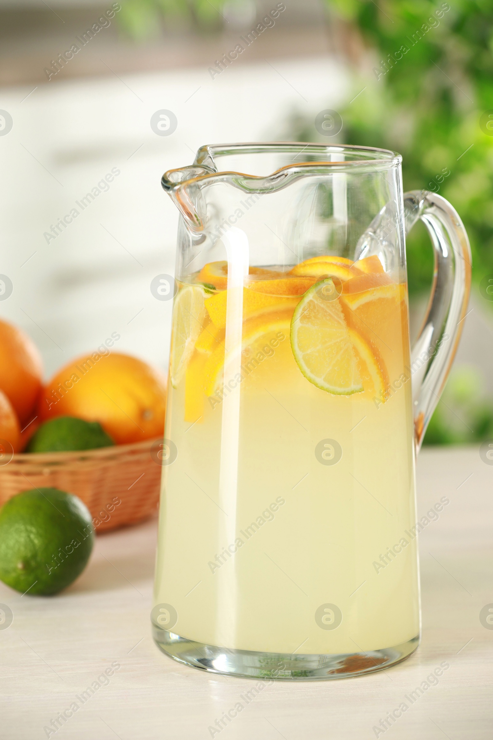 Photo of Refreshing lemonade with orange and lime in jug on white wooden table, closeup