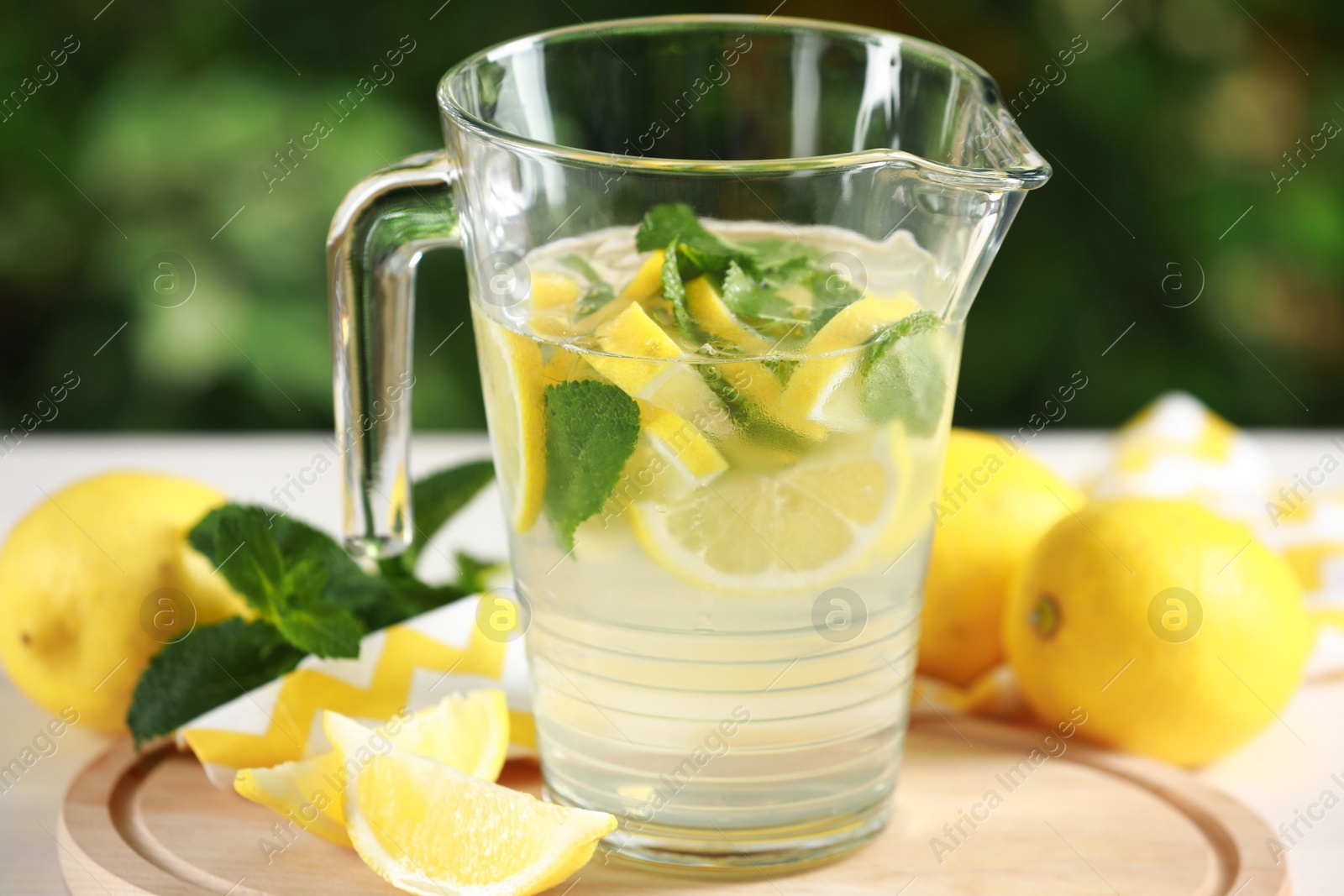 Photo of Refreshing lemonade with mint in jug among fruits on light table against blurred green background, closeup