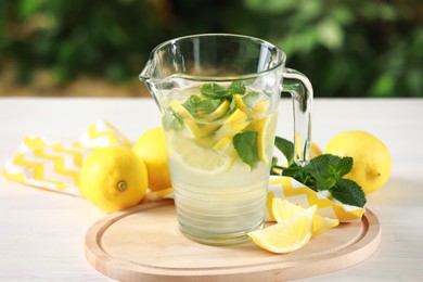 Photo of Refreshing lemonade with mint in jug on light wooden table against blurred green background