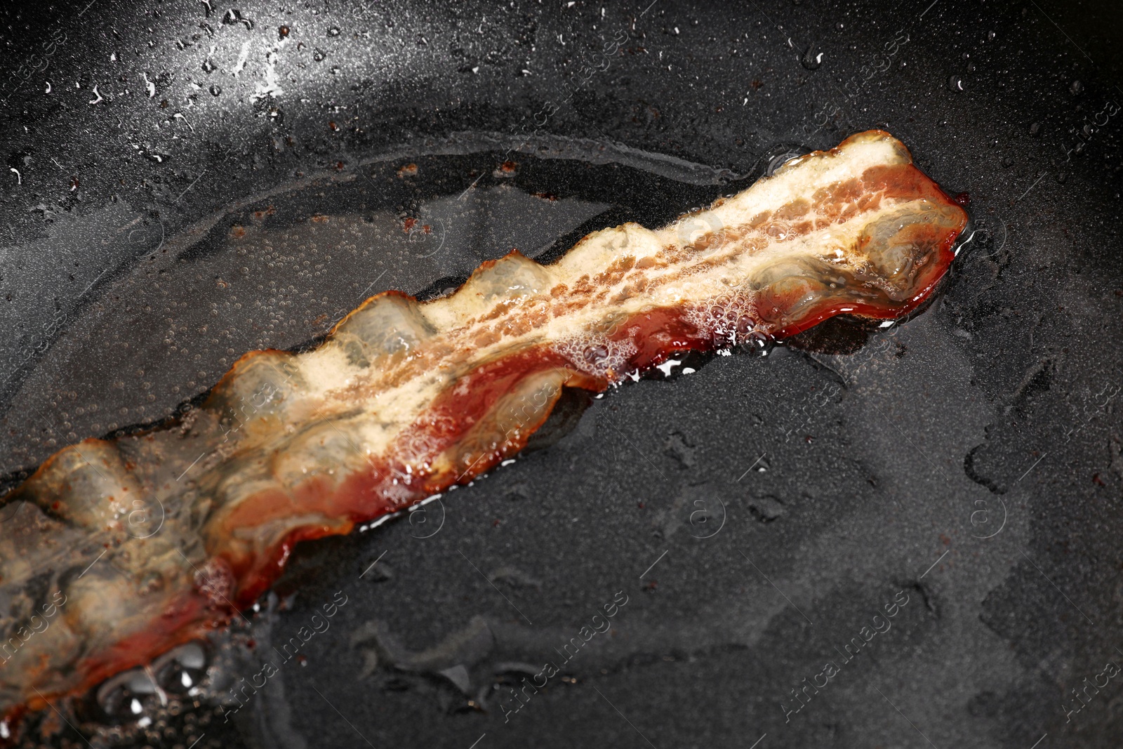 Photo of One slice of bacon frying in pan, closeup