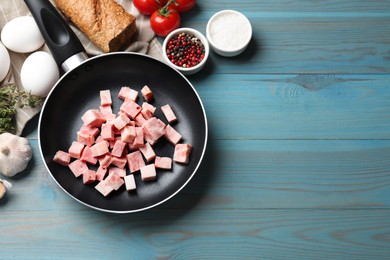 Photo of Pieces of fresh bacon in frying pan and products on light blue table, flat lay. Space for text