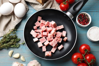 Pieces of fresh bacon in frying pan and products on light blue table, flat lay