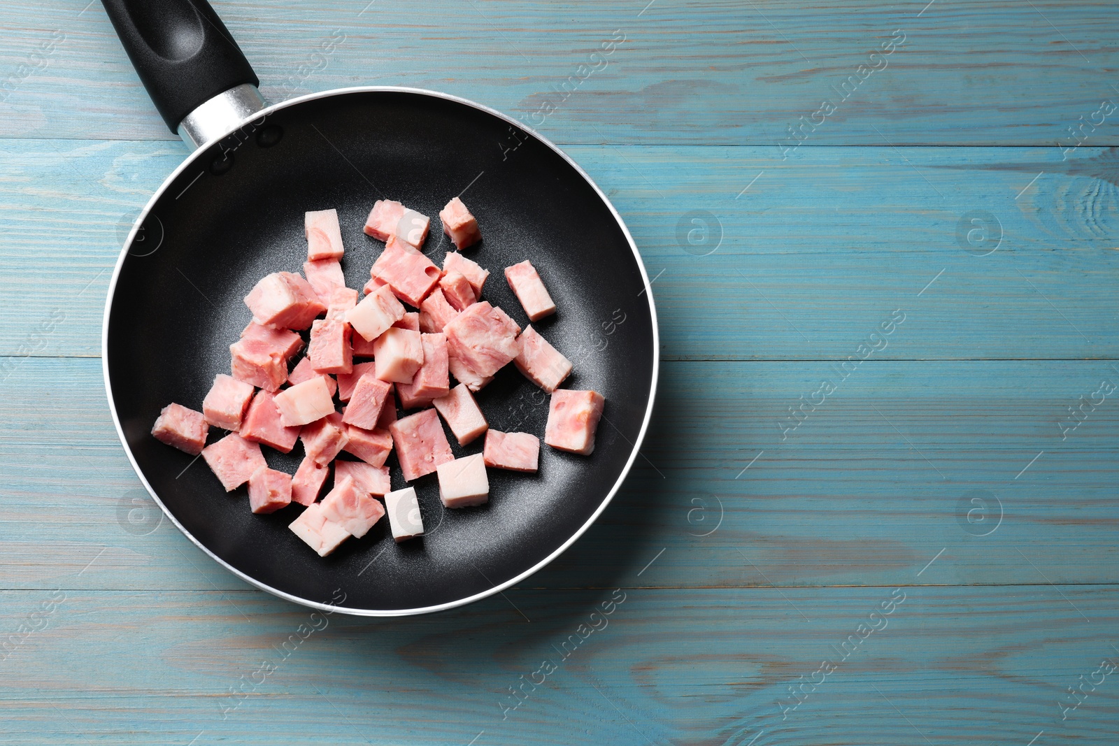 Photo of Pieces of fresh bacon in frying pan on light blue table, top view. Space for text