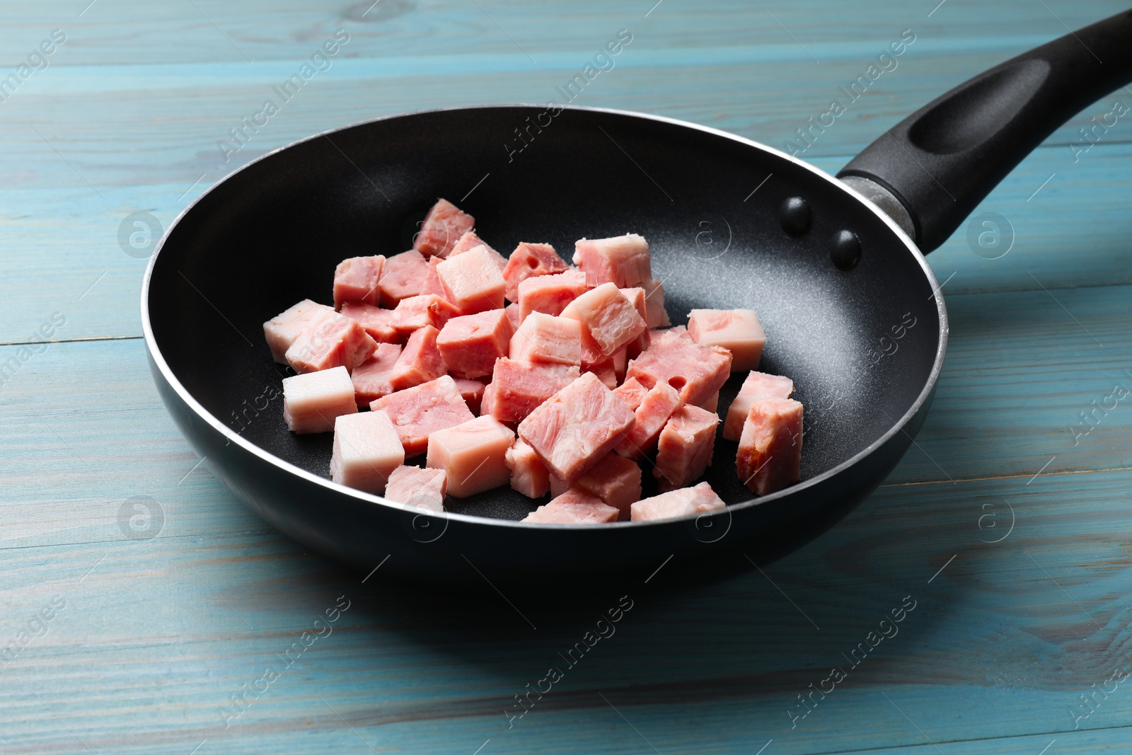 Photo of Pieces of fresh bacon in frying pan on light blue table