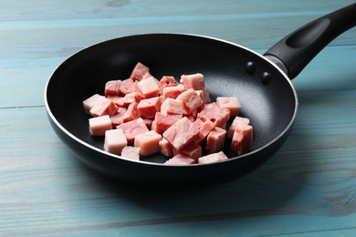 Photo of Pieces of fresh bacon in frying pan on light blue table